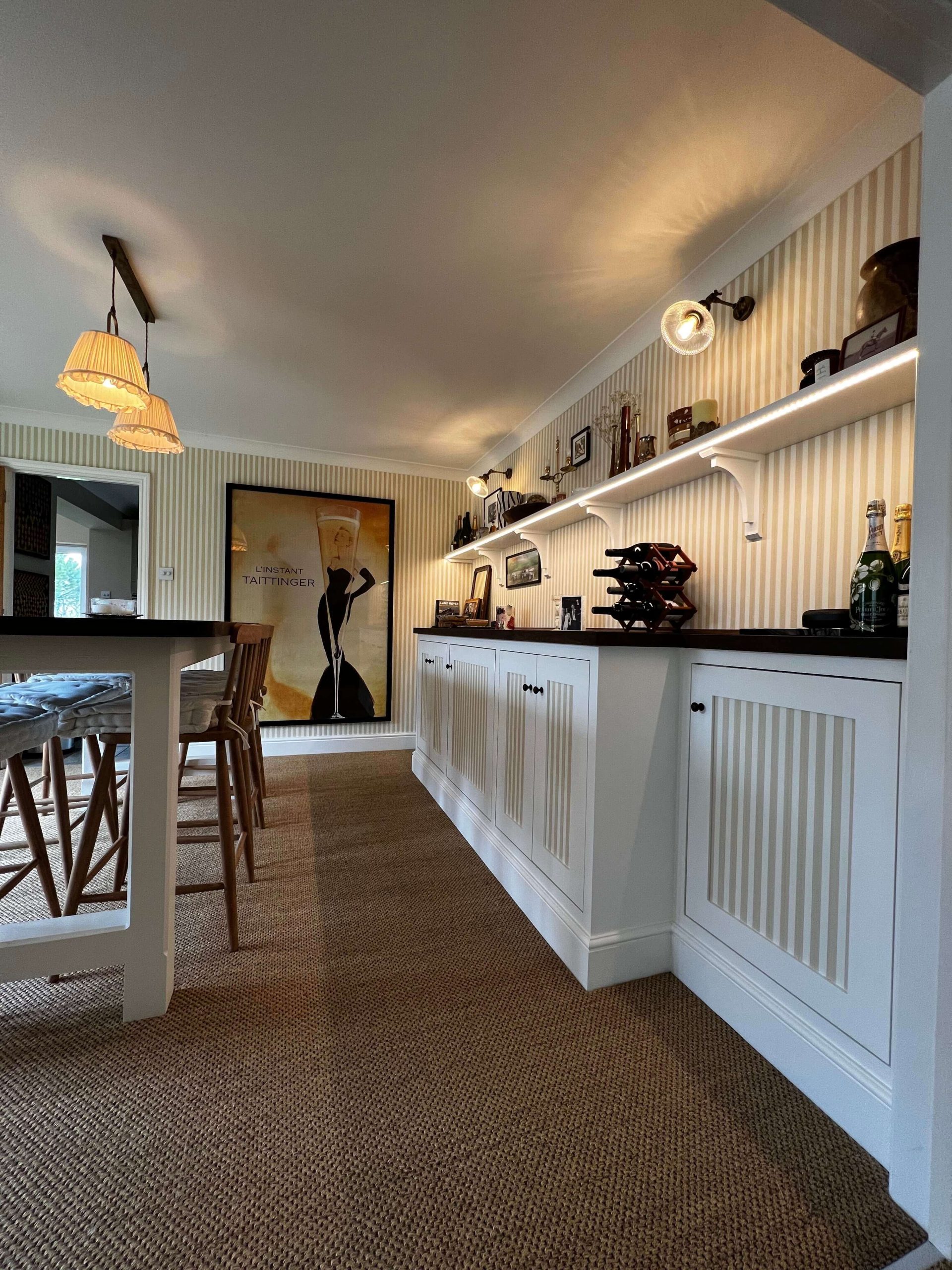 Built-in bar cabinetry with painted panelled doors, dark timber top and a lit display shelf above