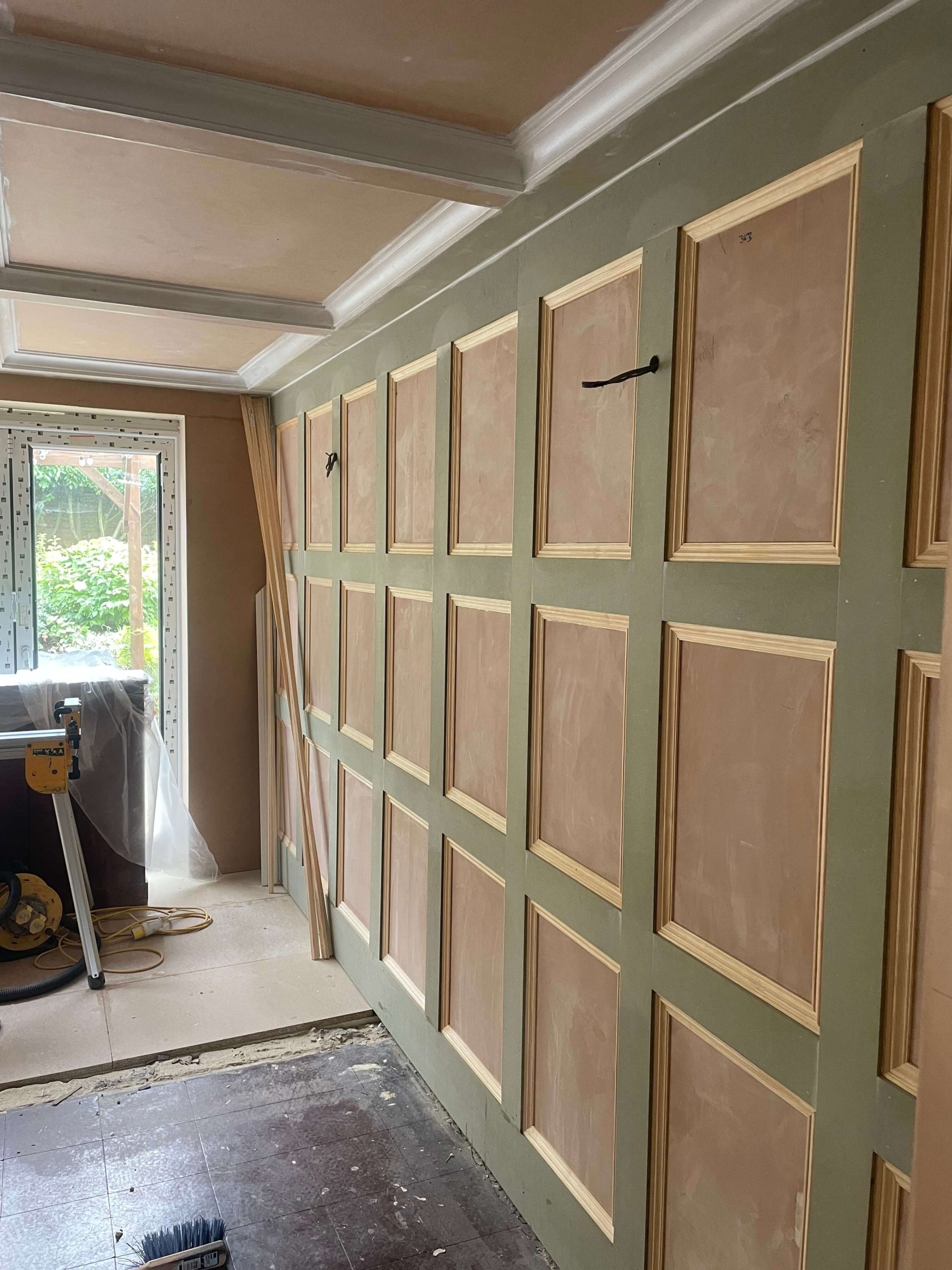 Wall panelling part-built, with primed panels and moulded beading fixed to a green painted wall