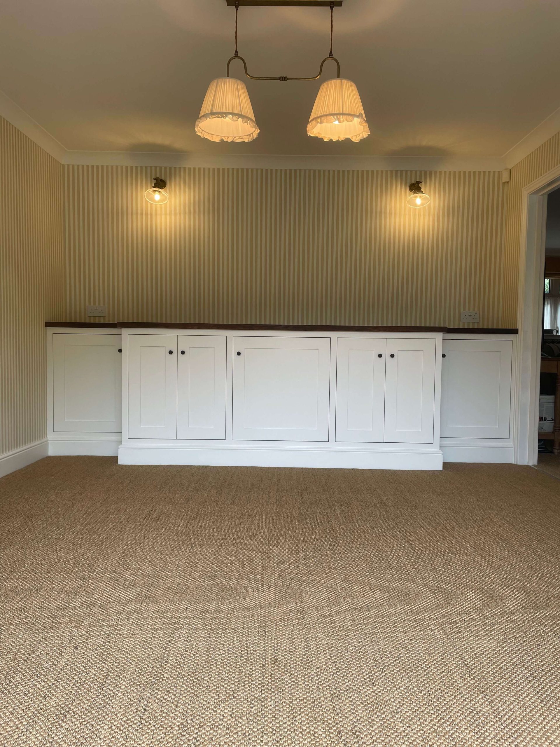 Built-in cupboards with painted shaker doors and a dark timber top against striped wallpaper