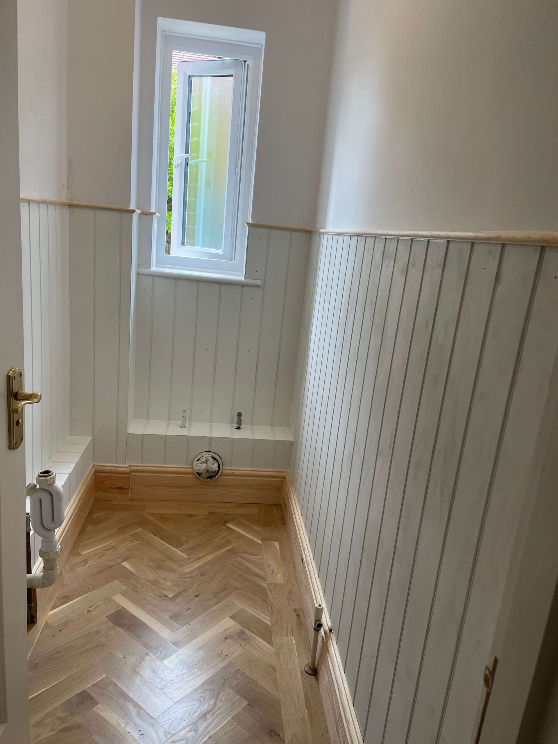 Cloakroom lined with white tongue-and-groove panelling and a herringbone oak floor