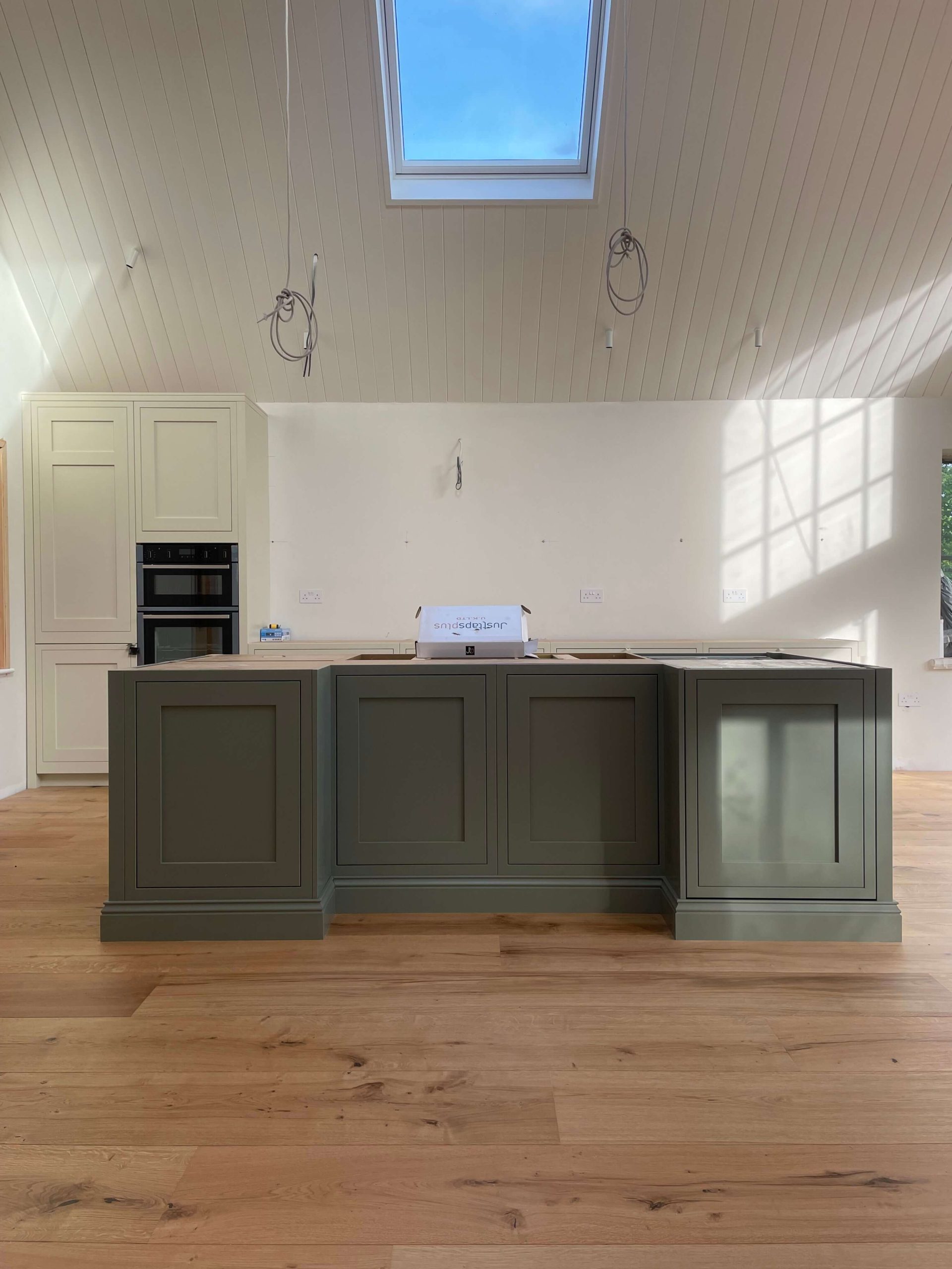 Kitchen island in deep green with shaker panelling, under a vaulted timber-lined ceiling
